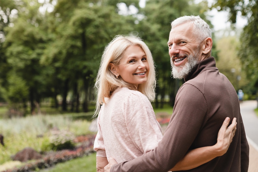 Smiling mature couple enjoying a walk in the park – Dentist Wenatchee WA Joyful senior couple embracing and walking together along a scenic path, showcasing bright healthy smiles – Dentist Wenatchee WA